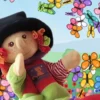 Marioneta de una brujita con sombrero negro, jersey rojo, falda verde y botas rojas, sentada en un tronco sobre un arroyo, rodeada de un torbellino de mariposas de colores y flores.